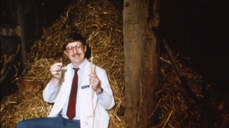 Francis Collins sits on a bale of hay and smiles