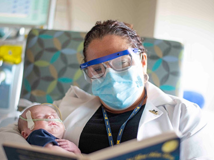 Nurse with goggles reading to sleeping baby pateint
