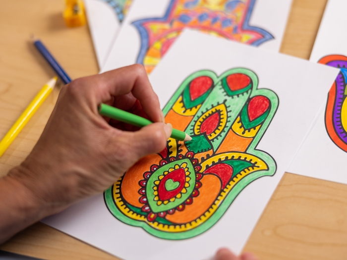 Hand holding green colored pencil coloring a Hamsa Hand project