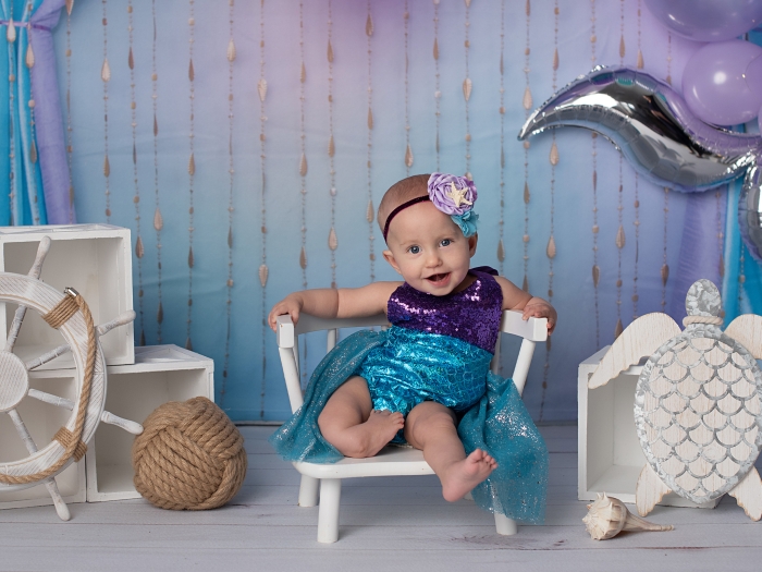 Baby sitting on chair smiling with purple background and props