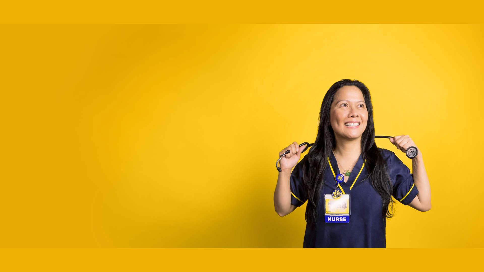 Female nurse smiling wearing maize and blue and holding stethoscope behind neck