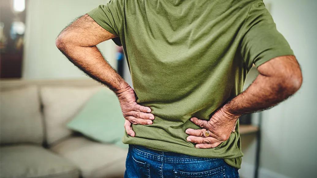The back of a man in a green shirt with his hands on his lower back