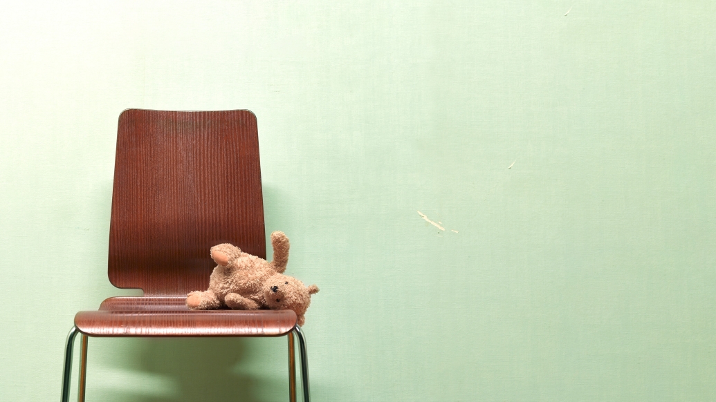 Empty chair with a teddy bear laying on it.