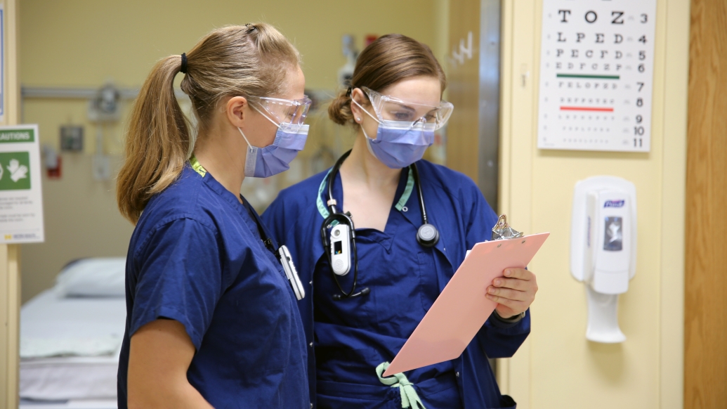Nurses looking at clipboard with goggles and masks on in clinic