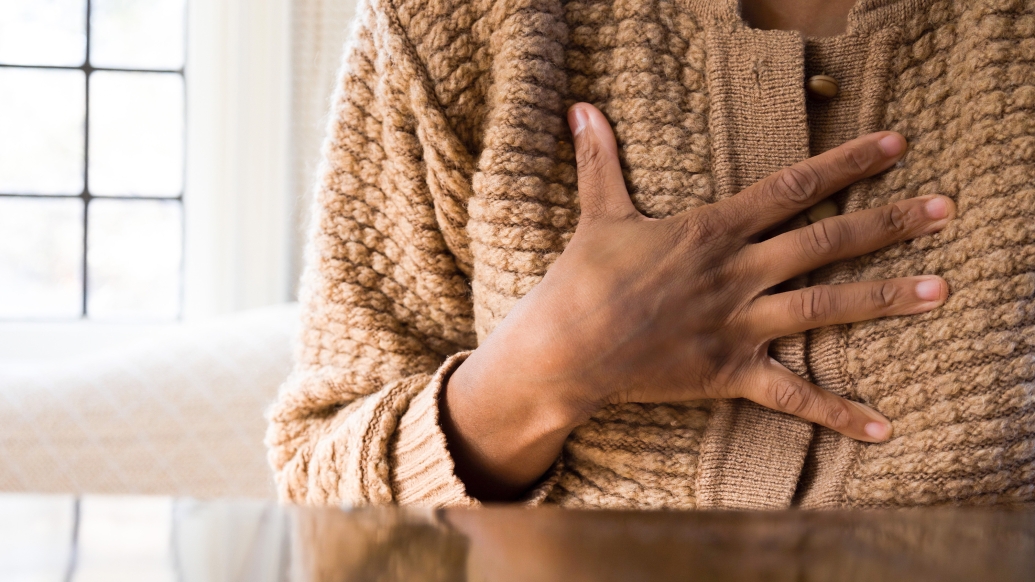 Woman holding her hand on chest wearing tan sweater