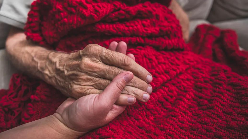 hand holding older hand over blanket