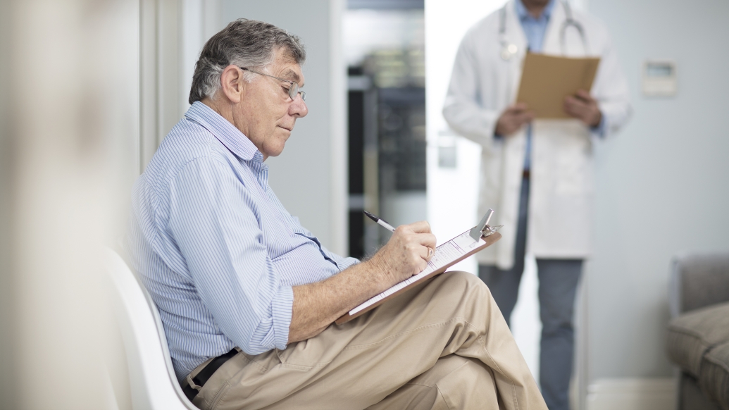 older man sitting filling out form in doctor's office