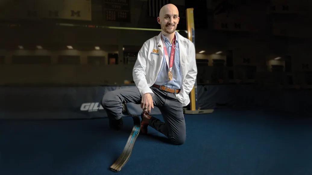 Man kneeling, wearing a doctor's white coat. His right leg has a prosthetic. 