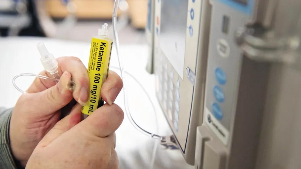 Close-up of a nurse's hands holding a syringe of ketamine that she is attaching to IV tubing
