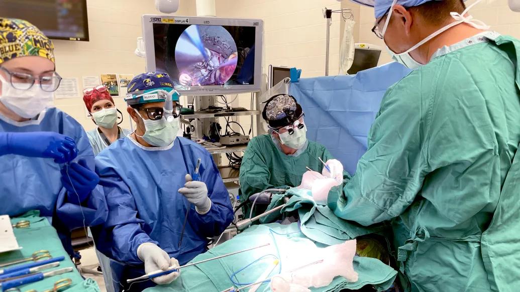 surgeons in OR with blue and teal scrubs with screen on and patient under teal sheet
