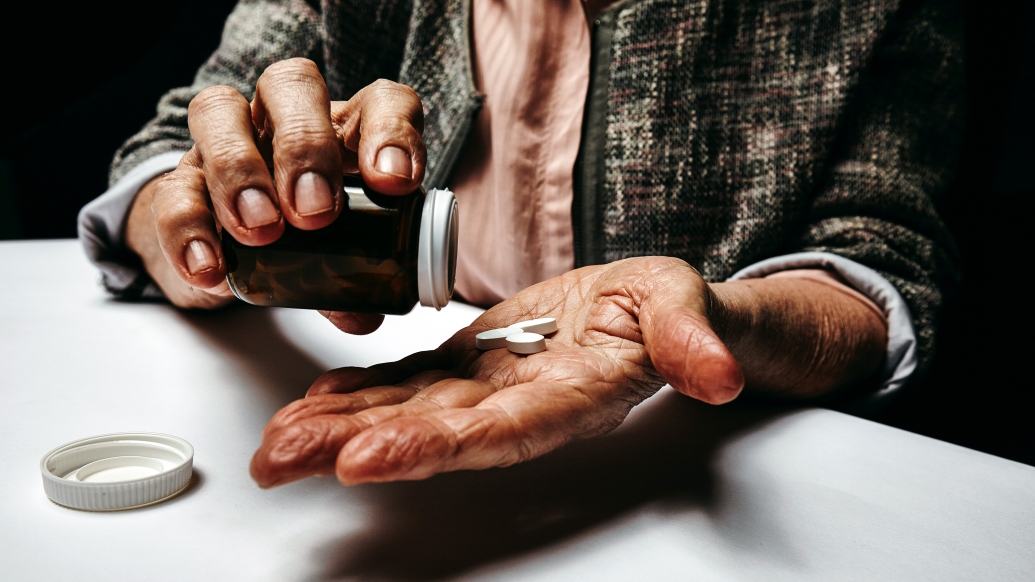 older person pouring pills into hand close up