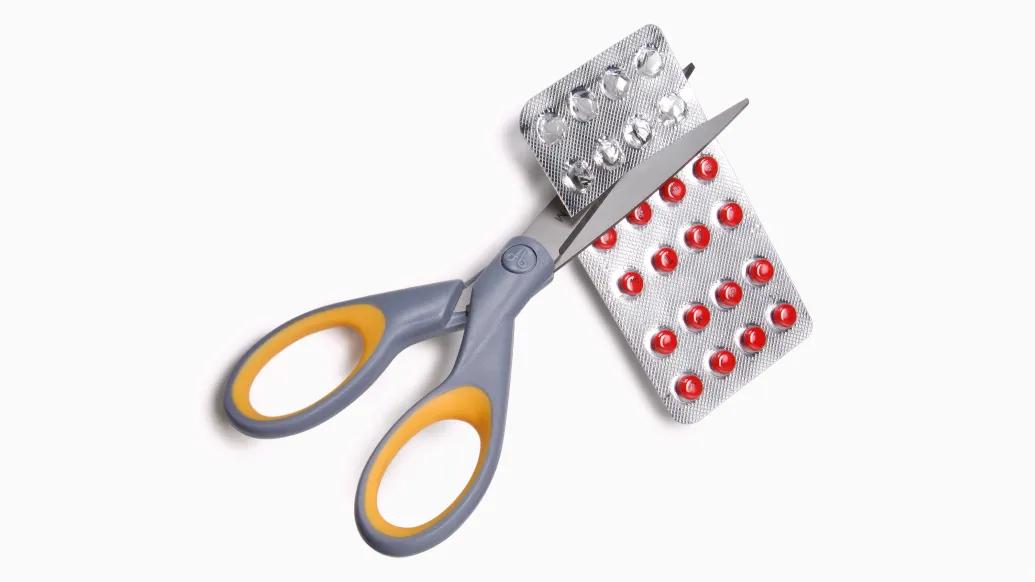 grey scissors cutting red pill back 