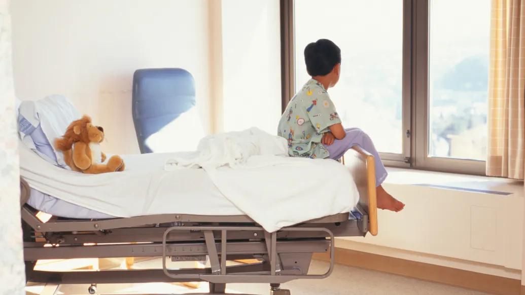 patient end of bed in hospital looking out window with stuffed animal on bed