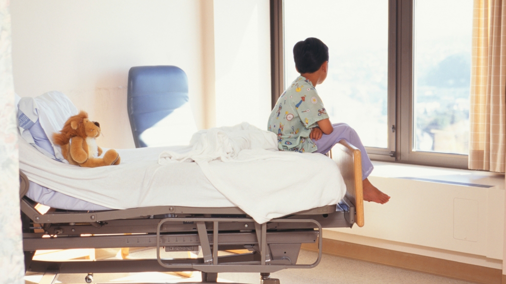 patient end of bed in hospital looking out window with stuffed animal on bed