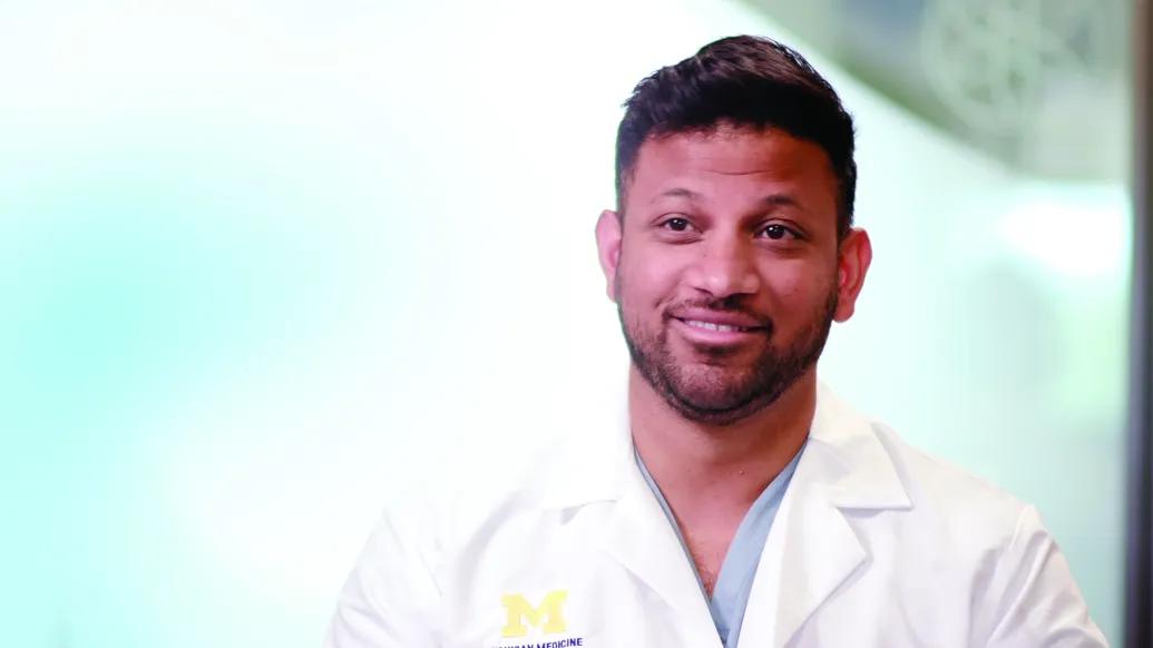 Video still of Shantanu Warhadpande wearing a white coat with a block M. 