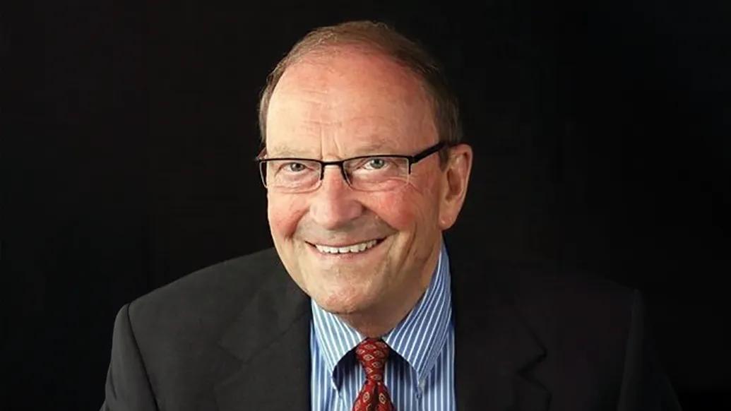 Portrait of Gary Randall wearing a black suit, blue and white striped shirt and red tie