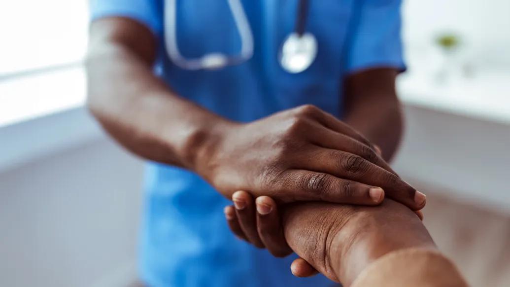 Health care provider with stethoscope holds patient's hand