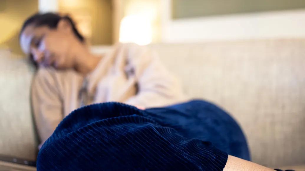 Woman sleeping on a couch holds her stomach, as if in pain