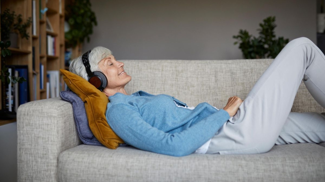 Older woman listening to music with headphones as she lays on a couch.