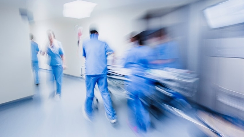 Blurred image of health care professionals in blue scrubs pushing a gurney down a hallway