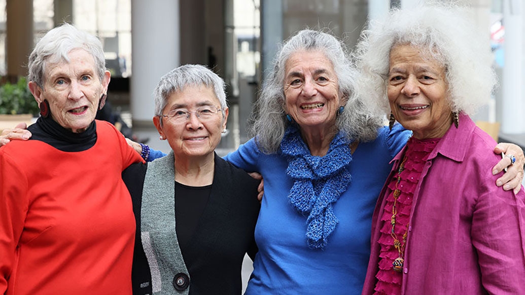 Four older women pose and smile