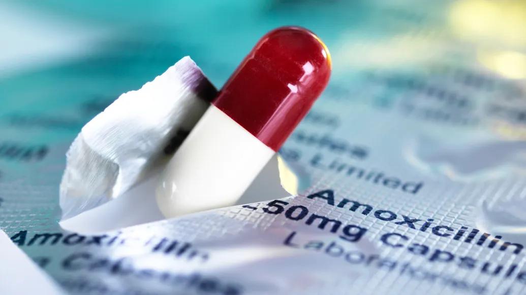 Pill capsule pushing through a paper with amoxicillin printed on it.