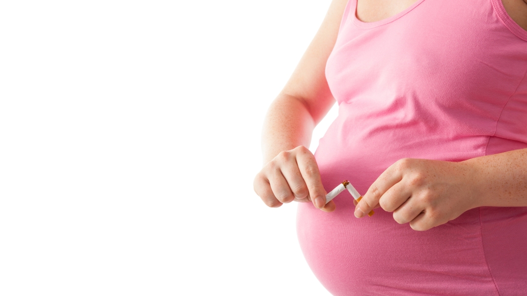 Pregnant woman in pink shirt breaks a cigarette in half in front of her stomach