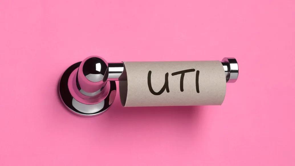 uti written on empty roll of toliet paper on a toliet paper holder with hot pink background