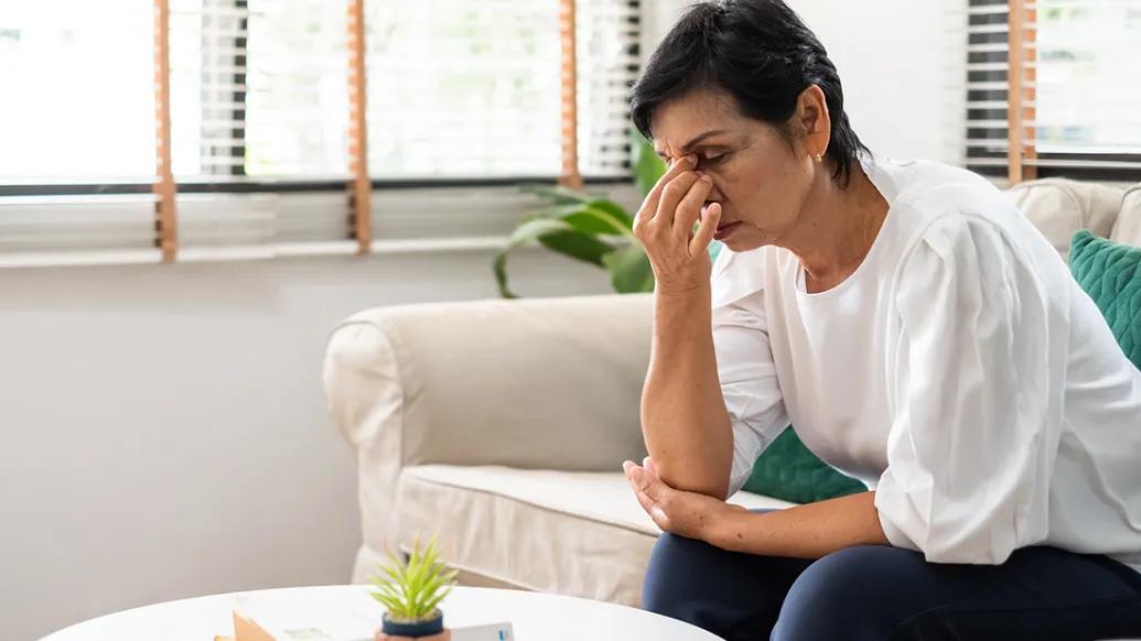 woman holding face looking stressed on white couch in white shirt dark blue pants