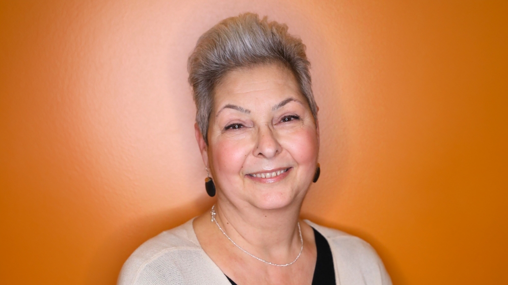 woman smiling with white short hair and earrings dark with orange background