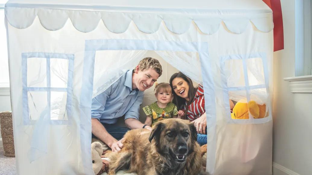 A family photo of Jake Ruduck with his wife, daughter, and dog. They are all sitting inside a white playhouse tent.