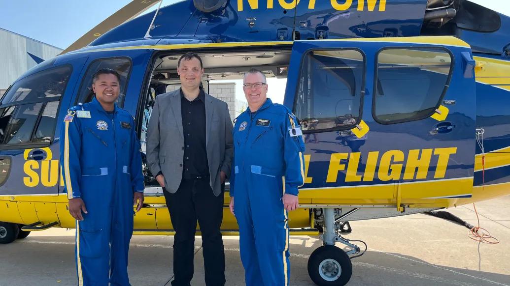 Survival flight pilots and person standing by helicopter smiling