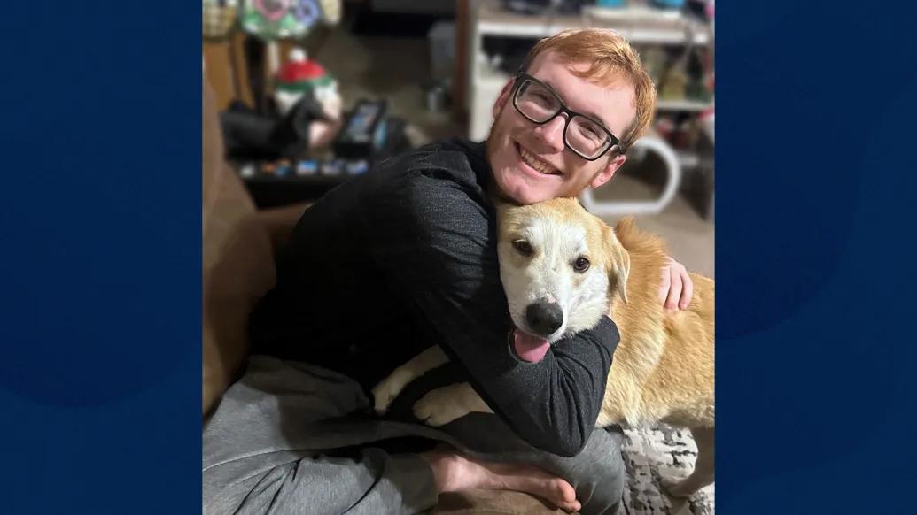 young adult male hugging blonde haired dog