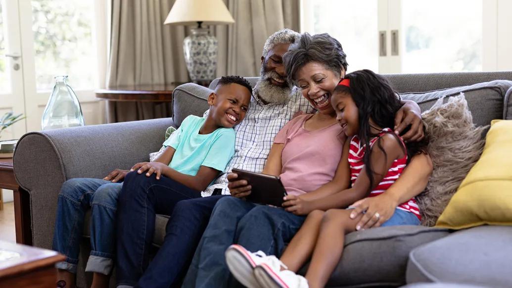 family of four sitting on couch in living room looking at an ipad laughing