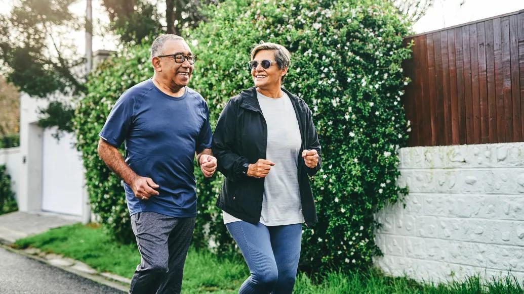 man and woman jogging outside with greenery behind them and fence on sidewalk