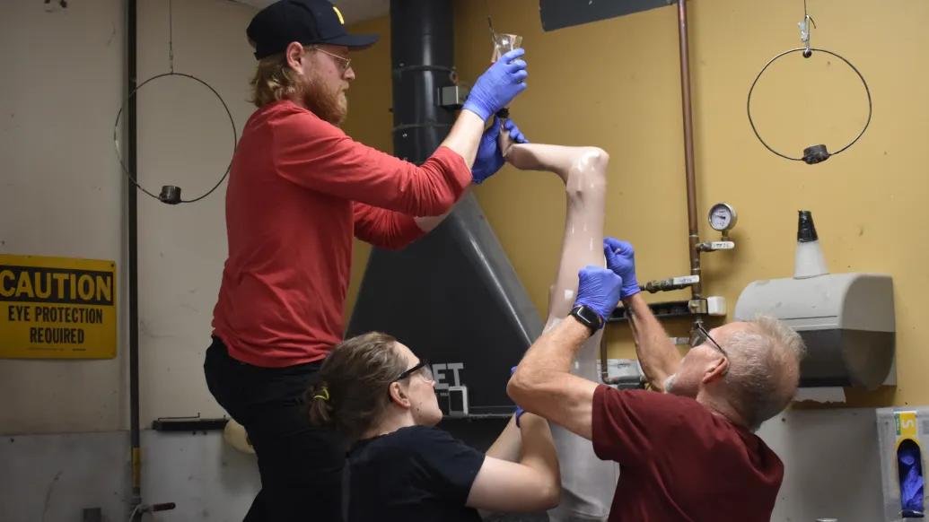 group working together on leg prosthetic in work room, one on top by foot and the other two on the calf of leg