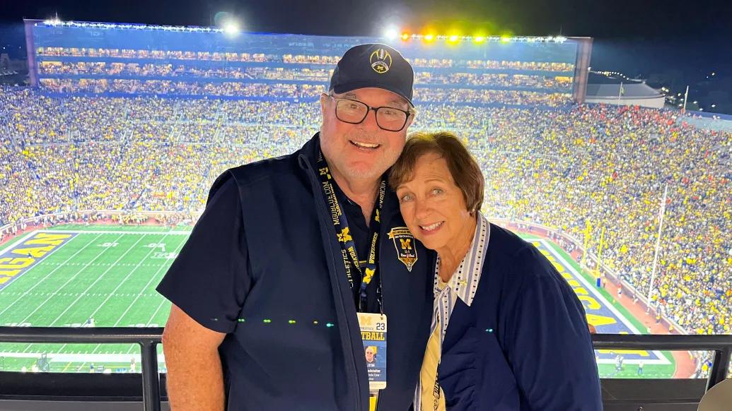 man and woman in front of stadium with crowd at UM