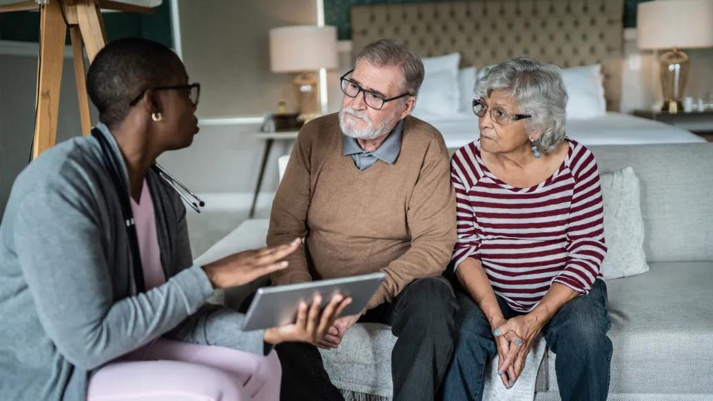 person talking to older couple on couch in living room