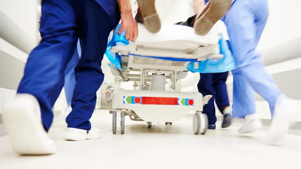 white sneaker feet in dark blue and light blue scrubs rushing a hospital bed into medical area