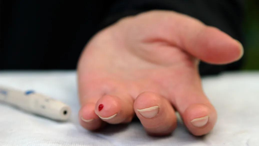 a hand on a table with a prick of blood on finger