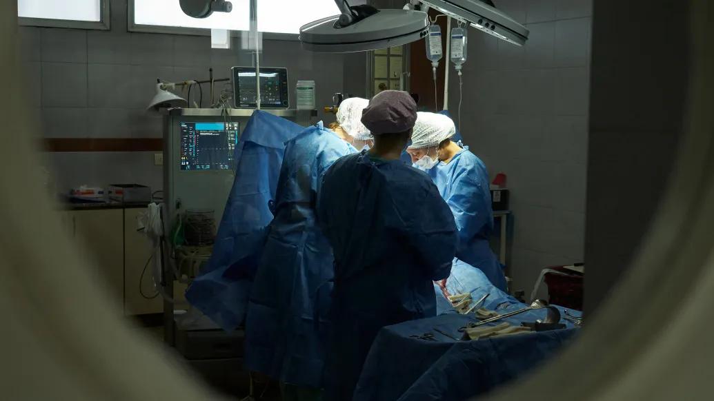 looking at surgeons operating in room with scrubs and scrub hats on through a door window