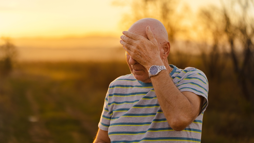 Older man wiping forehead during outdoor walk on hot day
