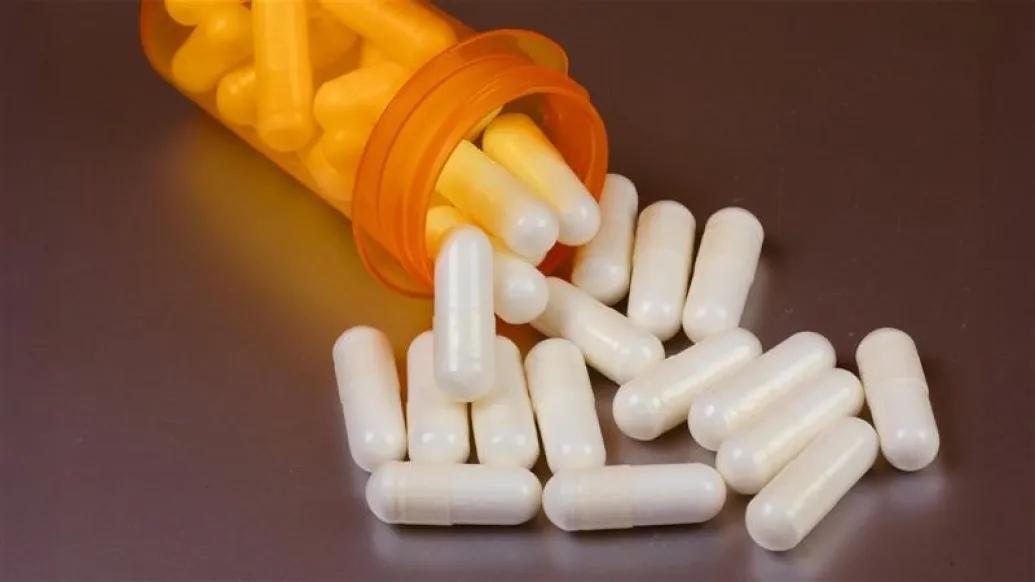 white pills falling out of orange pill bottle on a brown surface