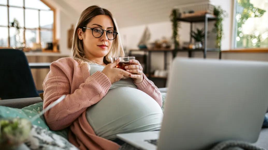 woman pregnant sitting holding tea and glasses on brown hair