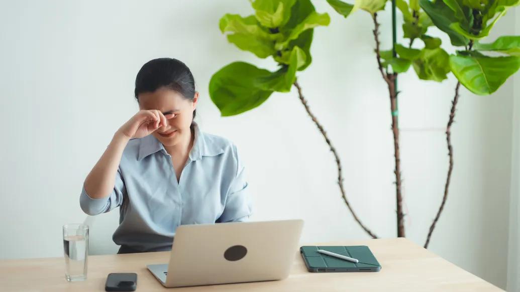woman sitting by laptop putting hands on eyes