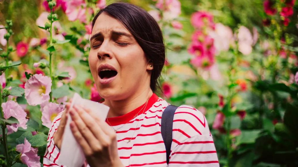 sneezing woman with flowers in background red shirt