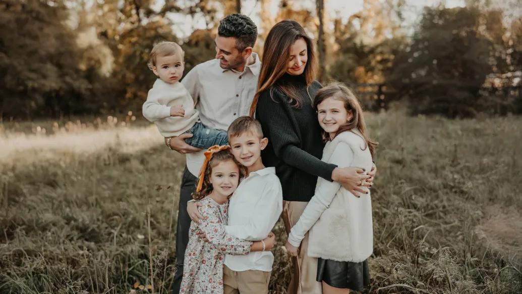 family photo mom dad and four kids in soft white beige and black clothes outside in field with trees behind