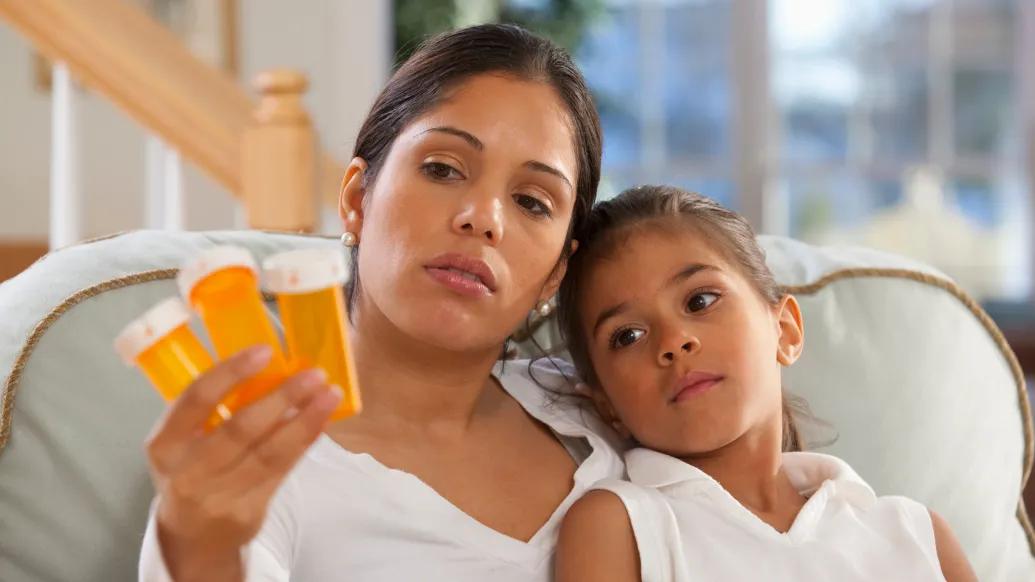 woman looking at orange empty pill bottles with daughter on couch