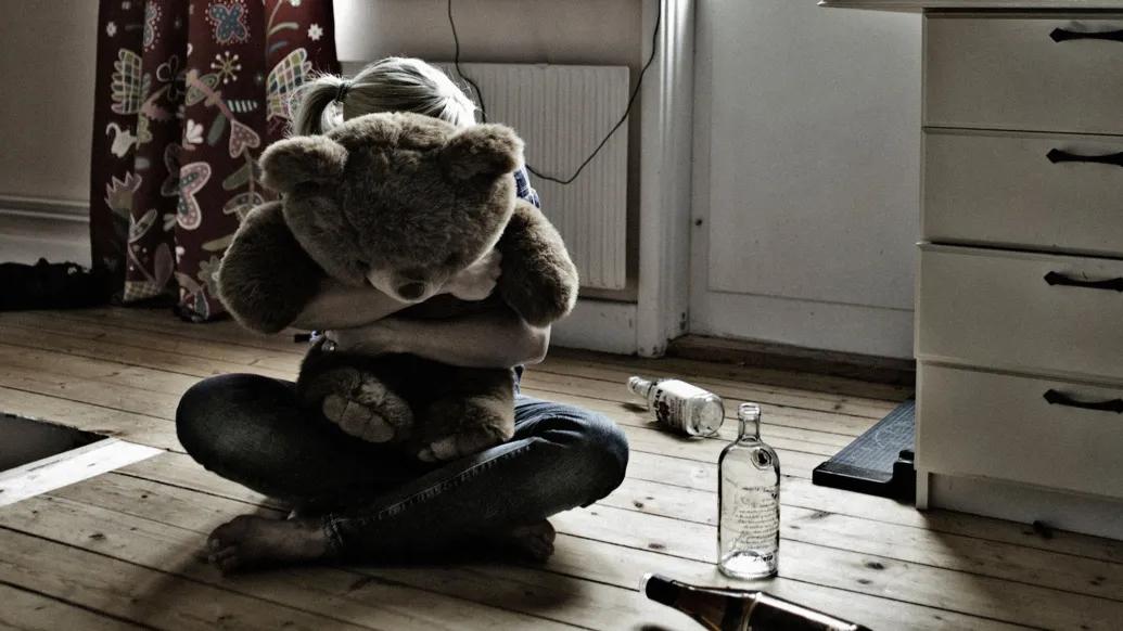girl hugging teddy bear with alcohol bottles on ground