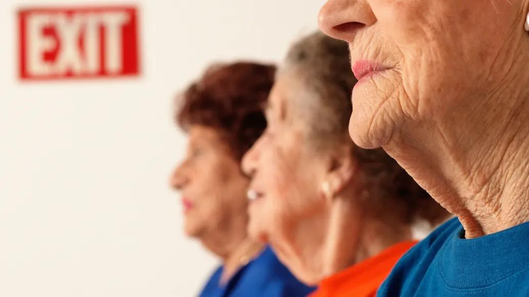 older women close up and blurred out by faces with an exit sign far away in red background and white writing